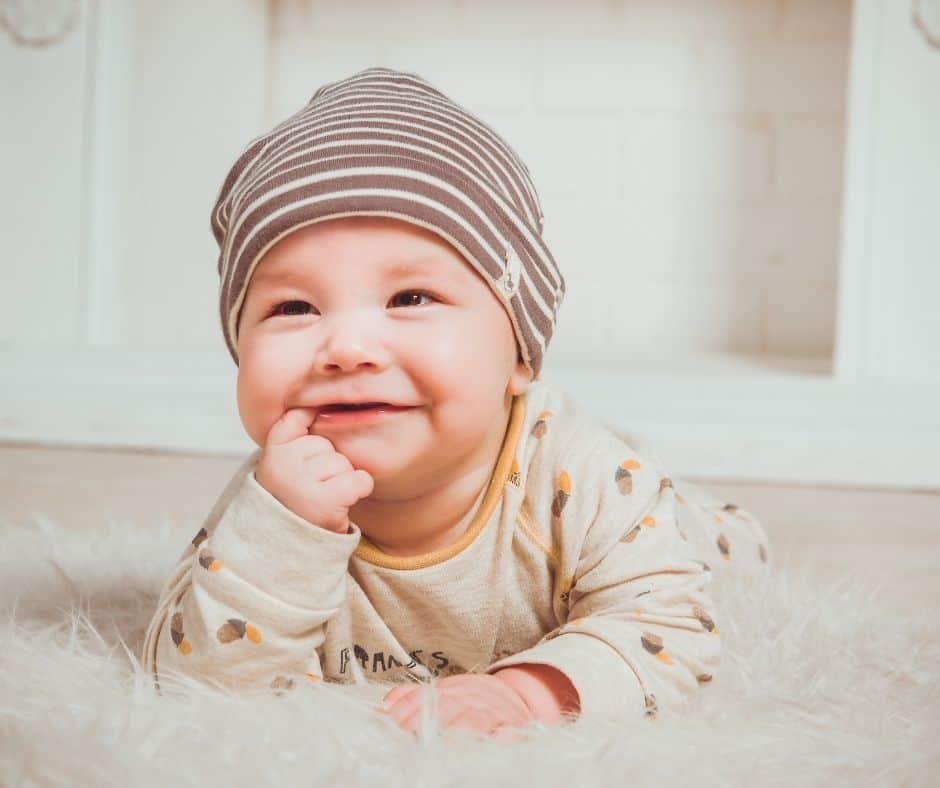 A baby in a striped hat laying on a rug.